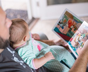 A father reads a storybook to their baby sitting in their lap. This could represent the bonds cultivated from working with a child psychologist. Search for child counseling in Branchburg, NJ and how child therapy in Branchburg, N J can offer support.