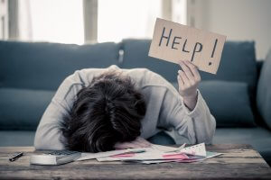 Woman with head down on a stack of papers on her desk, holding a sign up that says "help" due to anxiety. CBT therapy in Scotch Plains, NJ and online therapy in New Jersey can help alleviate anxiety symptoms in Fanwood, Cranford and Westfield, NJ.