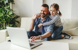 Happy father and daughter doing online therapy in new jersey on a laptop. Telehealth in New Jersey doesn't have to be difficult to access for parents and children with a child therapist in Westfield, NJ from Brave Minds psychological services.