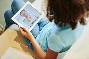 Teen Girl with an iPad sitting on her couch doing online therapy in New Jersey with Brave Minds Psychological Services from an online counselor who does telehealth in Scotch Plains, NJ 