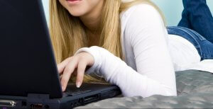 Teen girl laying on her bed looking on her laptop for online therapy in New Jersey at Brave MInds. Online counseling for teens in New Jersey is secure and convenient!