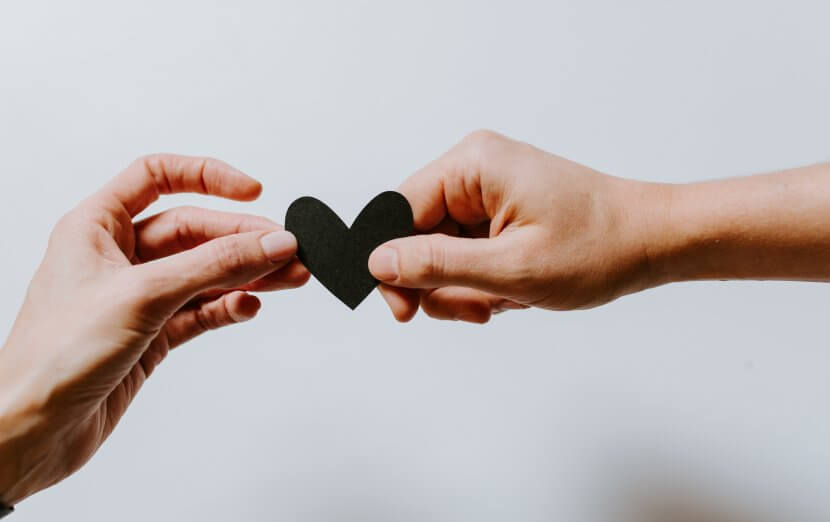 Two different hands hold either side of a black paper heart in front of a blank backdrop. Brave Minds Psychological Services offers couples counseling, marriage counseling, and more! Contact us today for support!