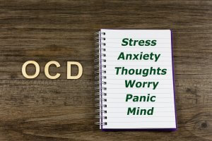 Word "OCD" on a wooden background with a notebook next to it with the words "Stress. Worry. Anxiety. Thoughts. Panic. Mind." for OCD Treatment in Westfield, NJ and OCD Treatment in Scotch Plains, NJ at Brave Minds Psychological Services Counseling Clinic. Online therapy in New Jersey is also available here!