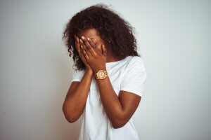 Young african american woman wearing t-shirt standing over isolated white background with sad expression covering face with hands while crying. You can get therapy for loss and grief in scotch plains, NJ at Brave Minds Psychological Services. Grief counseling in Westfield, NJ is available here!