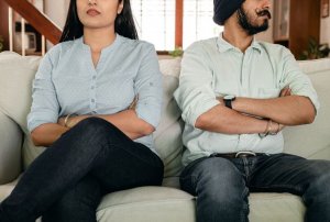 Couple sit on couch, both with their arms crossed. They are both in collared shirts and jeans. They are arguing with their therapist about what happened to make the spark go out in their relationship. Brave Minds Psychological Services offers couples therapy in Westfield, nj. Contact us today for support!