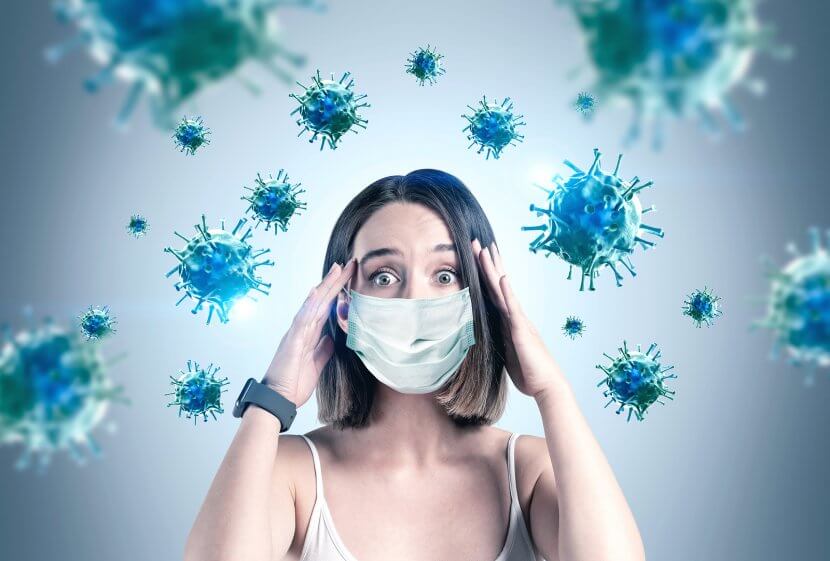 Scared young woman in medical mask standing over gray background with blurry red virus molecules. Coronavirus or COVID has an effect on postpartum in a pandemic. You can get birth trauma therapy or postpartum depression counseling in Cranford, NJ. Scotch Plains and Westfield, New Jersey 07076