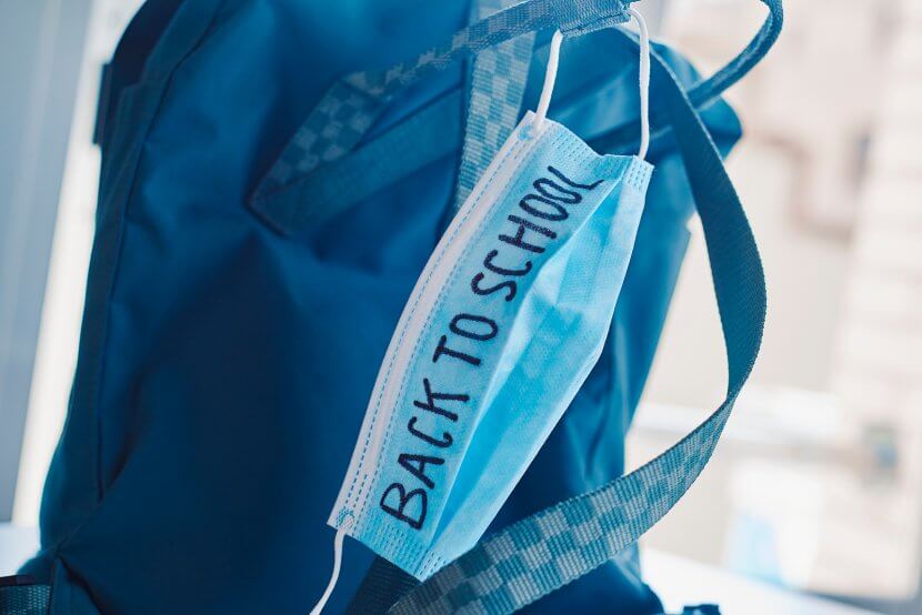 closeup of a green bookbag and a blue surgical mask with the text back to school written in it, depicting the need to prevent the infection at school in the covid-19 pandemic situation for virtual learning during COVID. You can get anxiety treatment in Westfield, NJ and Anxiety treatment in Cranford, NJ with Brave Minds in Scotch Plains, NJ