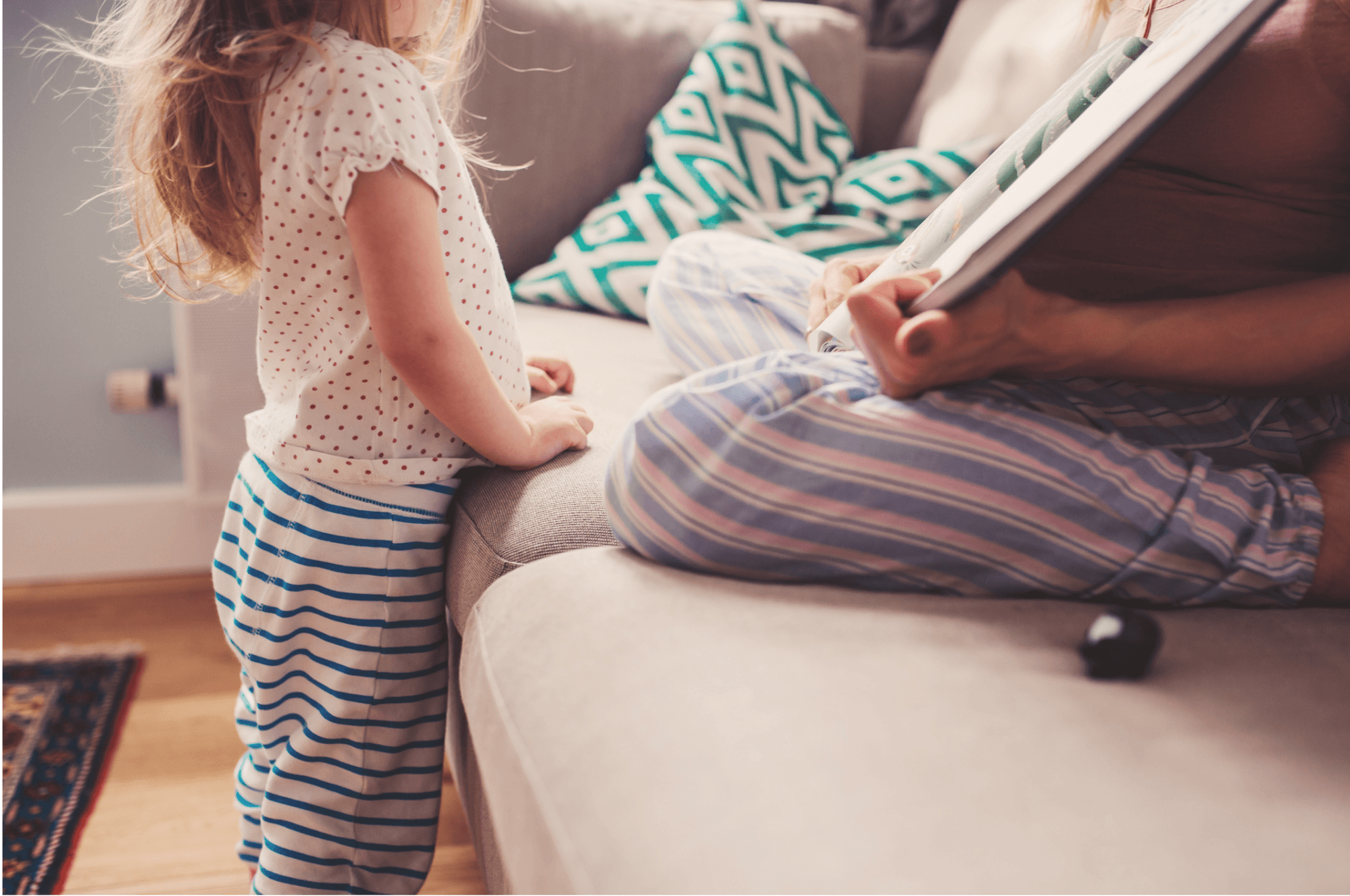 A light skin toned mother and daughter read a book together in their pajamas on the couch.