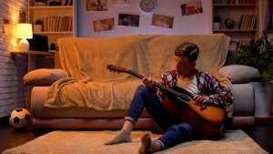 teen sitting on the floor of a bedroom playing guitar. he gets EMDR for teens with a teen therapist in Scotch Planes, NJ