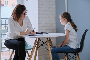 A therapist writes on her clipboard as she listens to the child across the table. This could represent a child therapist in Scotch Plains, NJ meeting with a client. Contact us to learn more about child therapy for anxiety and other services! 