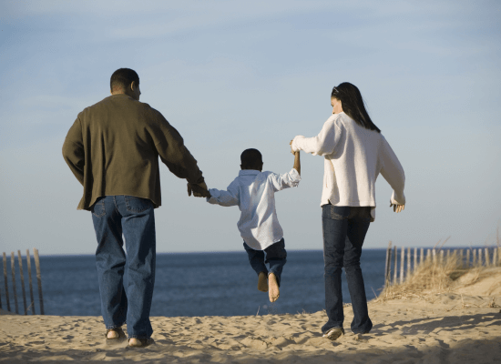 A man and a woman walk on the beach with their son. They are all holding hands.