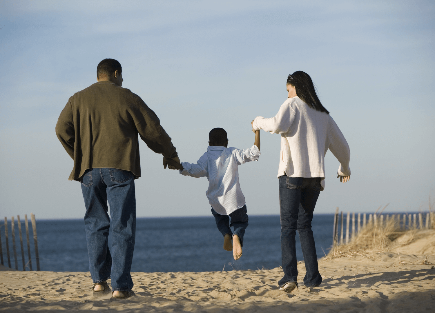 A man and a woman walk on the beach with their son. They are all holding hands.