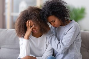 An upset teen is comforted by her mother on the couch. Counseling for teens in Scotch Plains, NJ can provide support for teens and parents navigating adolescence. Contact a teen counselor in Scotch Plains, NJ to learn about online therapy for teens.