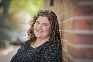 Kerry smiles as she stands against a brick wall for Brave Minds Psychological Services. Contact us to learn about sexual violence prevention in Scotch Plains, NJ. Online therapy for sexual assault in New Jersey can help you today! 07076