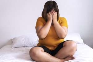woman sits on her bed and covers her face with her hands. She is learning more about rape culture and sexual violence from a therapist in Scotch Planes, NJ at Brave minds therapy, Learn more about sexual violence support today. 