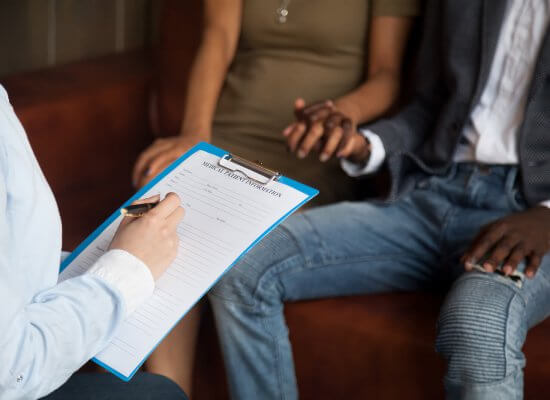 A couple sit holding hands as a therapist writes something on their clipboard. This represents couples therapy in Scotch Plains, NJ. Couples counseling can help your relationship thrive. Learn more about marriage counseling in Westfield, NJ and other services today!