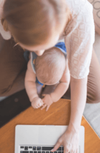 A new mother holds her baby on her lap while she uses her laptop computer.