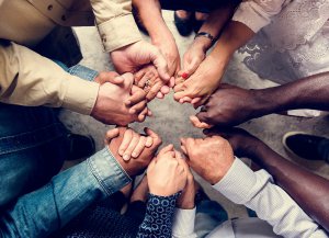 Image of a diverse group of people holding hands in a tight circle. Online group therapy in New Jersey. Attend loss and grief support group with us in Scotch Plains, NJ 07076. 