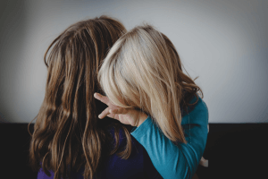 A brunette mother is holding her blonde child. The child's head is cuddled into their mother's neck.