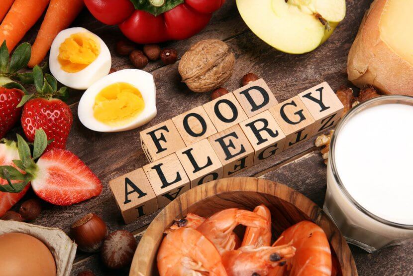 Image of food allergy spelled out in wooden blocks surrounded by food that could cause anaphylactic reaction in New Jersey. Thus showing that just the image of foods can cause food allergy anxiety but a trauma therapist can help with that.