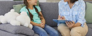 Image of a smiling child sitting on a couch with a child therapist. This shows the environment that a therapist or psychologist will create in child therapy for anxiety in Scotch Plains, NJ.