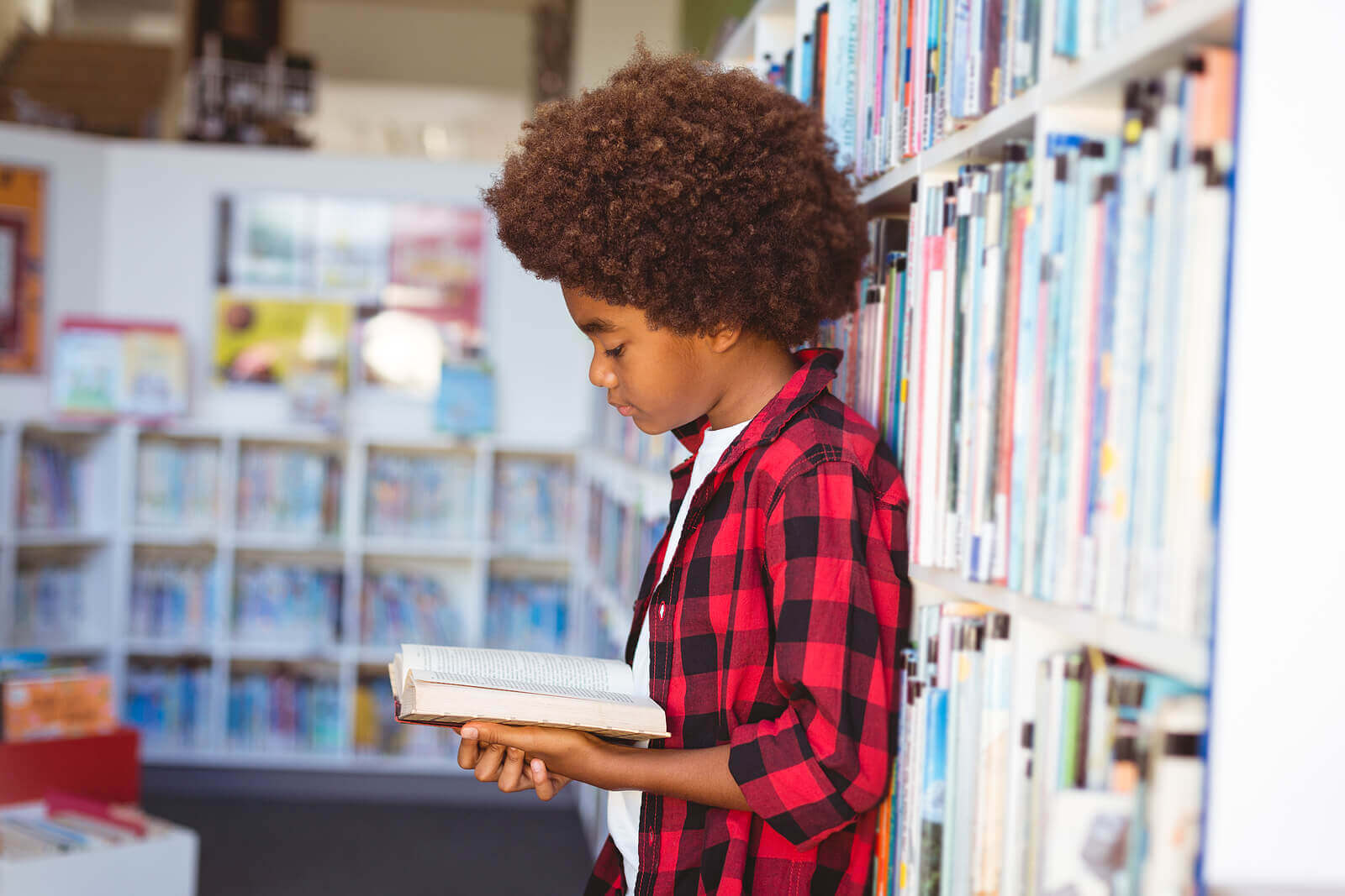 Image of a boy in a red shirt reading a book at a school library. Showing how selective mutism can affect how kids socialize at school. However through child counseling a child psychologist can make a plan for the school that support your kid.