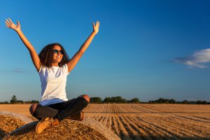 A teen smiles while sitting on a hay bale in an open field. This could symbolize how online therapy for teens can offer support from anywhere in the state. Learn more by searching "teen counselor scotch plains, nj" or "online therapist new jersey" today.