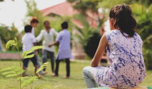 Shows a young child watching other children play while they sit out. Represents how selective mutism treatment in scotch plans nj can help children manage their anxiety and social skills.