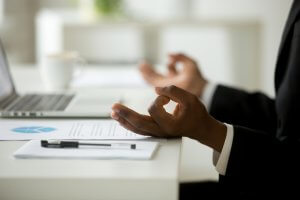 A close up of a worker holding their hands in a meditation pose at their desk. Learn how a perfectionism therapist in Scotch Plains, NJ can offer support with addressing burnout and balance. Westfield NJ counseling can offer support via online therapy for college students in New Jersey today.