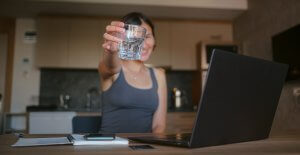 A woman smiles while holding a cup of water towards the camera. This could represent a more healthy work-life balance cultivated by working with a perfectionism therapist in Scotch Plains, NJ. Learn more about online therapy for college students in New Jersey by searching for Westfield NJ counseling today.
