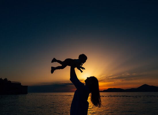 A mother holds their baby above their head against the light of the rising sun. Learn how a child therapist in Branchburg, NJ can offer help for new parents. Search for “single parent scotch plains, nj” to learn more about parenting help today.