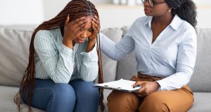 A woman holds her head in her hands while a woman with a clipboard comforts her. Learn more about the support that Scotch Plains therapy can offer by searching for child therapy in Branchburg, NJ and the difference between therapy and psychiatry.