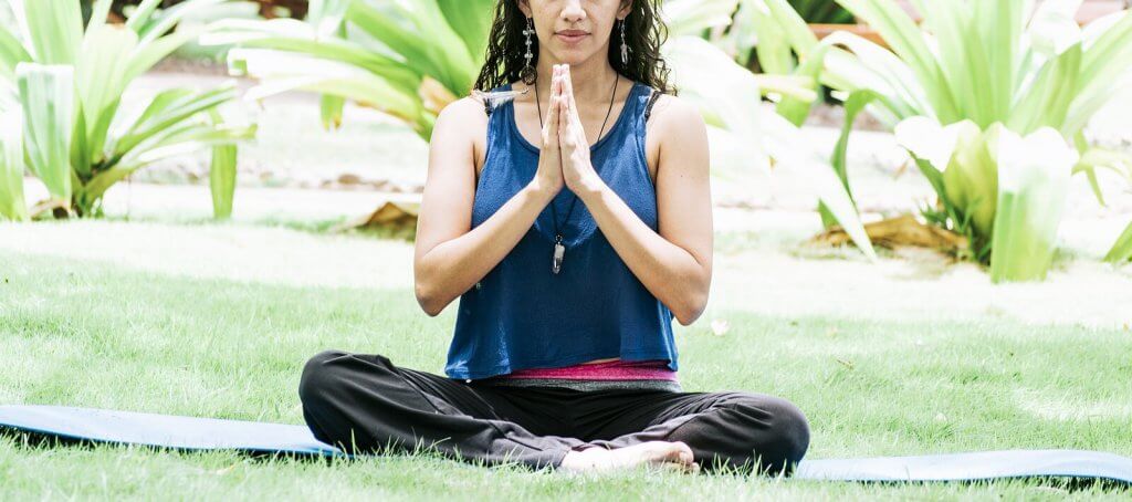 A woman sits with hands together outside on a yoga mat. Learn tips on addressing food allergies and anxiety by searching for "therapist Branchburg, NJ" for support with teens with food allergies New Jersey. an anxiety therapist in Branchburg, NJ can teach new mindfulness techniques.
