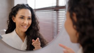 A woman smiles while pointing at herself in the mirror. This could represent the self boundaries created after online group therapy in New Jersey. Learn more about counseling in Branchburg, NJ.