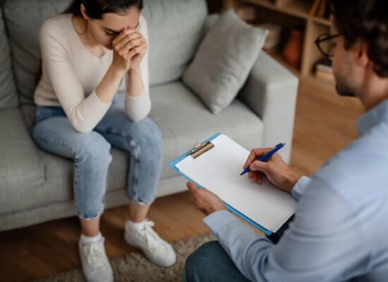 A woman hands her head while sitting across from a person with a clipboard. This could represent the support an equestrian therapist Branchburg, NJ can offer. Learn more about the help equestrian therapy in New Jersey can offer by searching for EMDR therapy in Branchburg, NJ today.