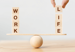 Wooden blocks spelling out the words "work" and "life" balancing on opposite sides of a scale, depicting a work-life balance. It can be difficult to manage the balance and flexibility when also navigating infertility and treatments. Seek a therapist to help with these challenges in Scotch Plains or Branchburg, New Jersey.