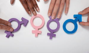 Hands holding four of the gender identity symbols. From left to right they are bigender in purple, female in pink, transgender in purple, and male in blue. Learn how to support your transgender child with a counselor that understands transgender youth.