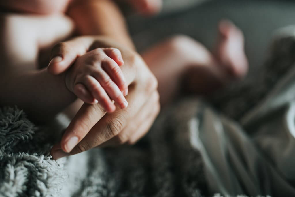 An infant clasping a mom's finger with a soft blanket in the background, reminiscent of the warmth and unity found in an online support group in NJ. Call us to learn to find empowerment in motherhood.