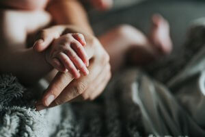 An infant grasping a mom's finger with a soft, fuzzy blanket in the background.