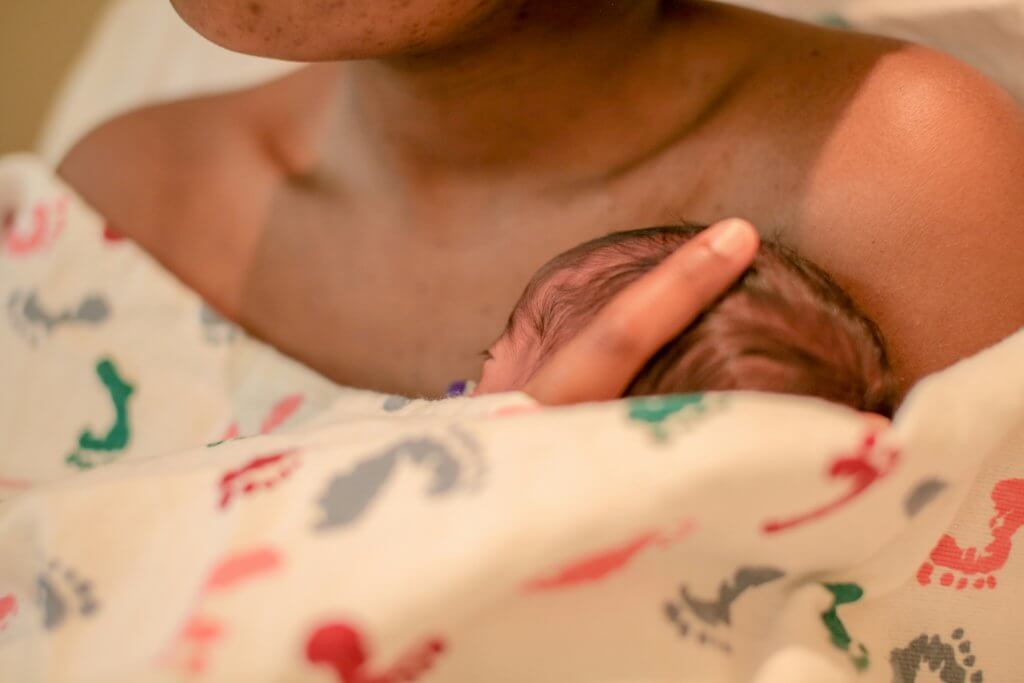 An infant resting against a mom's chest, covered by a blanket with colorful prints. Becoming a mom is a life-changing experience. Consider joining an online support group in New Jersey to help with this transition.