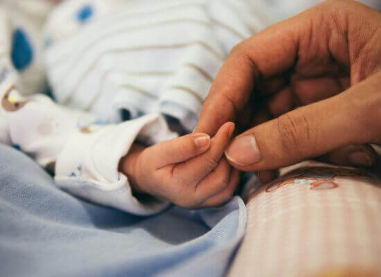 An infant's hand grasping a mom's finger in support of an online group. Consider joining an online support group in New Jersey to help