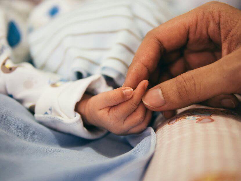 An infant's hand grasping a mom's finger in support of an online group. Consider joining an online support group in New Jersey to help