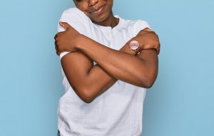 A close-up of a woman hugging herself while smiling. This could represent the self-love cultivated after receiving help from a moms support group in Branchburg, NJ. Search for online therapy in New Jersey and other services.