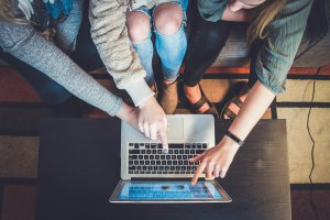Three people from a mom support group collaborating online using a laptop on a wooden table.