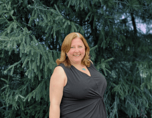 Woman smiling in front of evergreen trees.