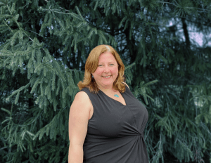 A smiling woman posing in front of green foliage.
