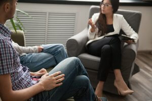 A woman holding a clipboard getstures with her hand while sitting and talking to a couple. This could represent the support offered from a family therapist in Branchburg, NJ to address family issues. Learn how online therapy in New Jersey can offer support by seaching for therapy branchburg, nj today.