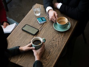 Two people having a meeting over coffee, with a smartphone and passport on the table.