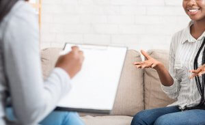 Woman in a striped shirt gesticulating during a conversation with another person holding a clipboard. This could represent how food allergies and anxiety can be addressed with an anxiety therapist in branchburg, nj. Learn more about anxiety treatment Fanwood, NJ and other services today.