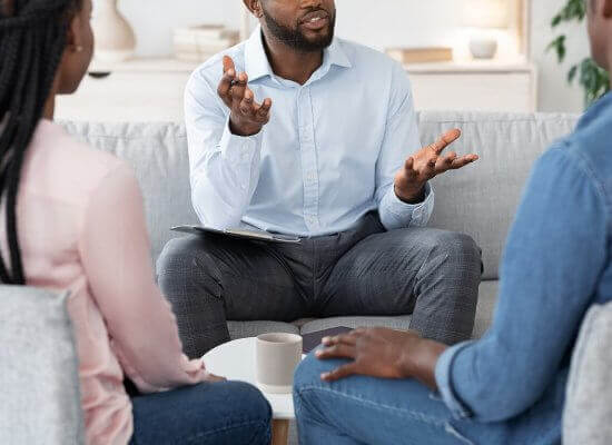 A person talks to a man and woman sitting across from them while gesticulating with their hands. learn how a family theapist in Branchburg, NJ can offer parenting help. Search for therapy branchburg, nj to get in contact with a group therapist in Scotch Plains, NJ today.